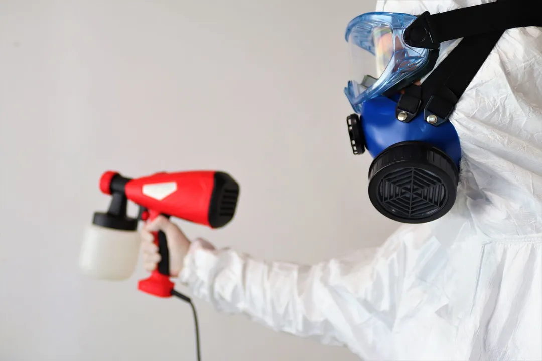 Technician in a protective suit and full-face respirator holding a fogging sprayer